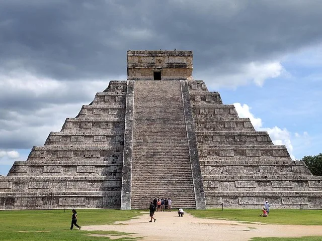 Touristen stehen bei bewölktem Himmel am Fuß des El Castillo in Chichén Itzá.