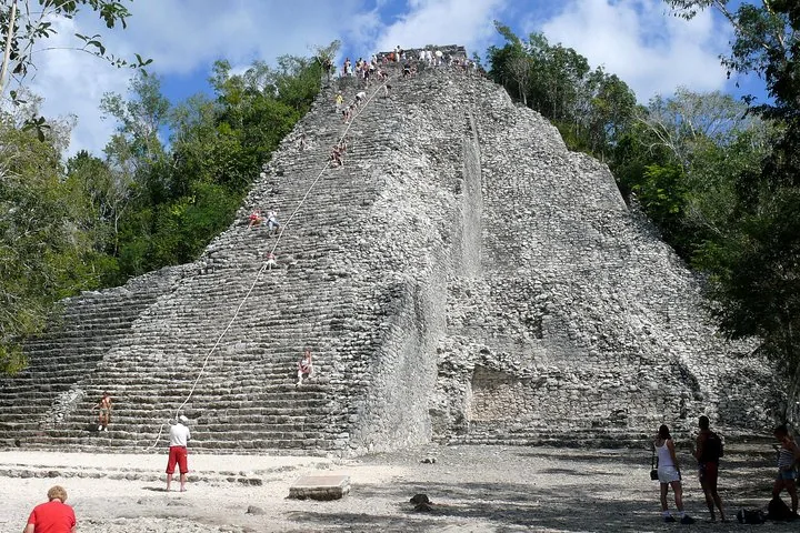 Touristen erklimmen eine steile antike Steinpyramide an einem zentralen Seil.