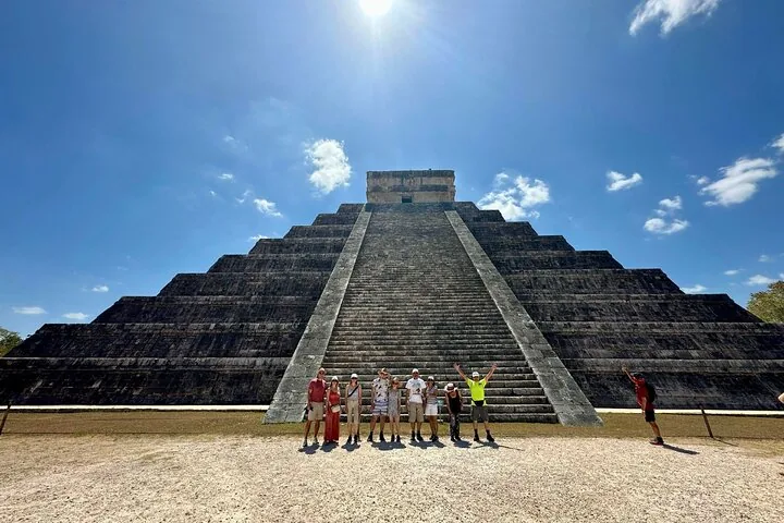A group of tourists pose at the base of the El Castillo pyramid.